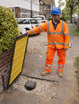 Worker lifting an Oxford Plastics LowPro 12/8 trench cover on a footpath