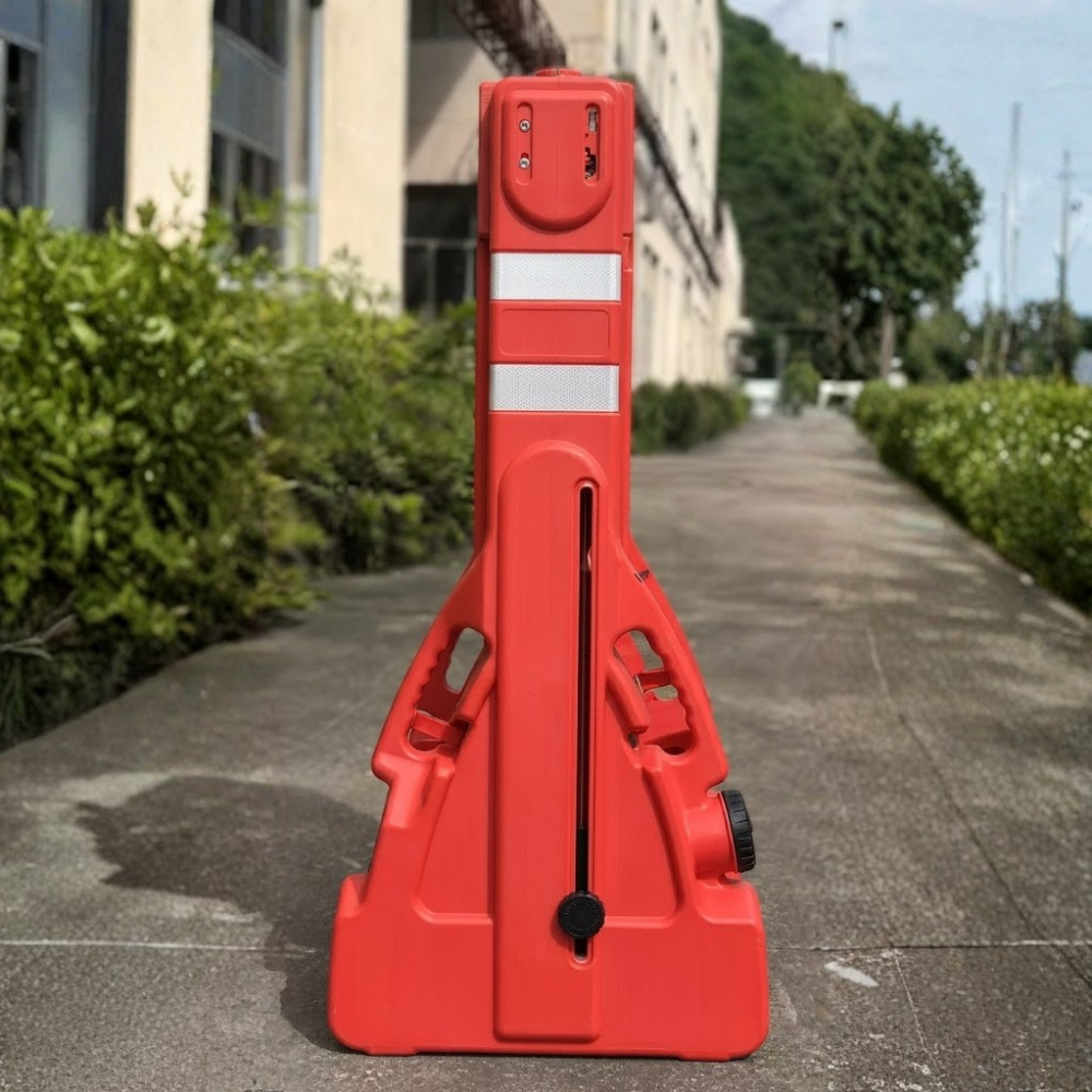 Red traffic barrier on a sidewalk with buildings and greenery in the background