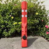 Red traffic barrier with reflective stripes on a pavement surrounded by greenery and flowers.