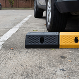 Two speed bumps on a street with a car's tire partially over one of them.