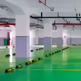Green floor with yellow safety cones in a large indoor area with white pillars and red pipes.