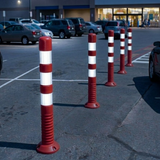 Red and white striped bollards in a parking lot with cars and a store in the background.