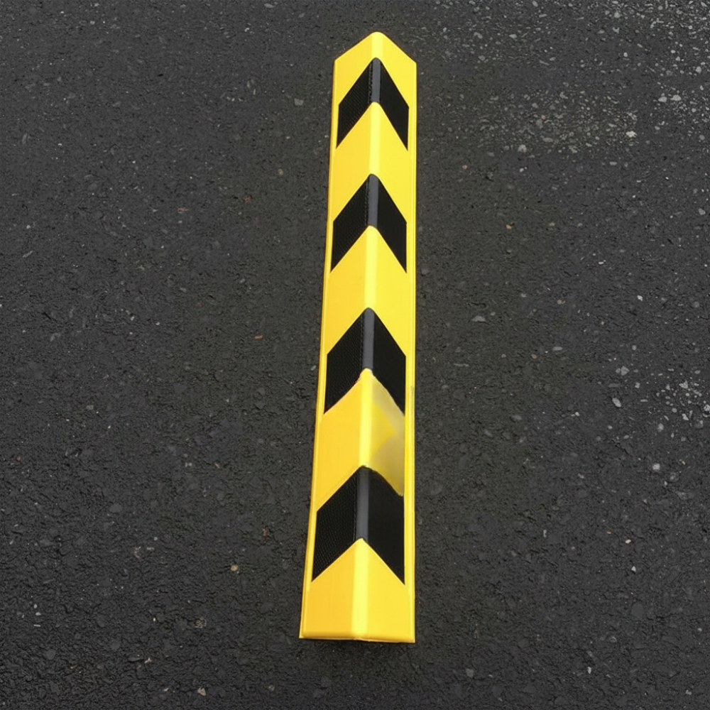 A yellow and black chevron-patterned safety corner guard on a dark asphalt surface.