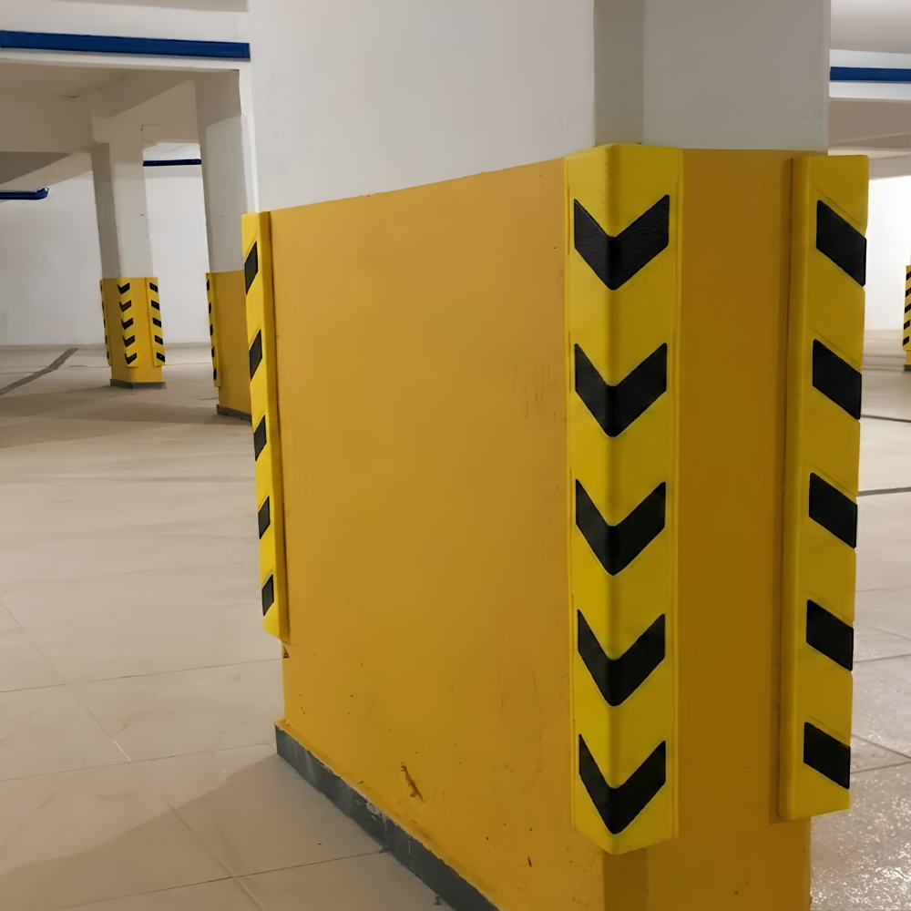 Yellow parking structure corner guard with black chevron markings on a white pillar in an indoor parking garage.