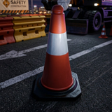 Orange traffic cone on a road with construction barriers and vehicles in the background