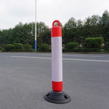 Red and white bollard on a road with trees in the background