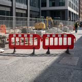 Red barriers blocking a street with construction equipment and materials in the background.