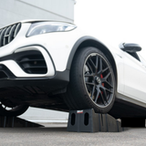 White car with a black tire on a raised platform, likely a car jack, with a blurred background.