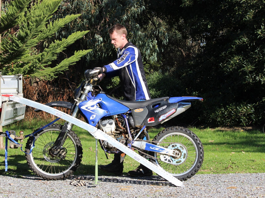Rider lining a blue dirt bike up straight behind a Heeve folding motorcycle ramp on a ute