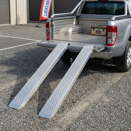 Two truck ramps extended from a pickup truck bed with a visible brand logo in the background.