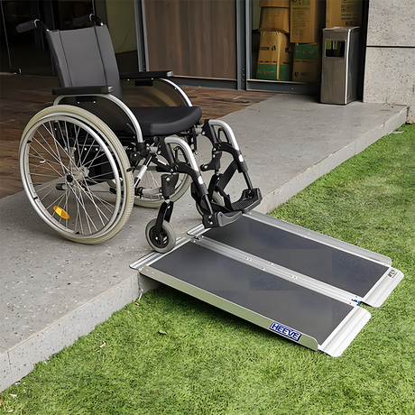 Wheelchair positioned on the Heeve aluminium single-fold ramp on a grassy outdoor step, illustrating its usability for wheelchair accessibility