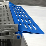 A close-up of a blue metal ramp with a slotted design, attached to a silver metal frame, set against a white background.