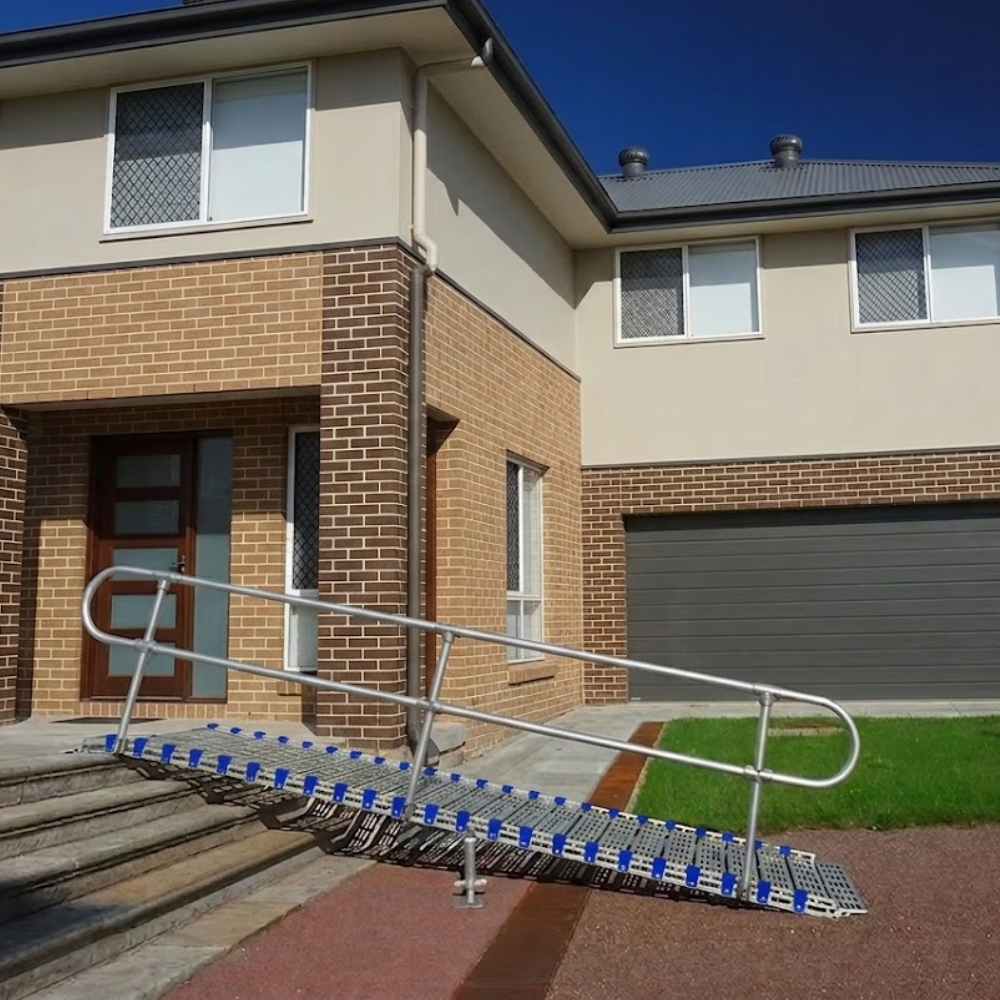 A metal stair ramp with blue grip pads and silver metal handrails installed on the front steps of a residential house.