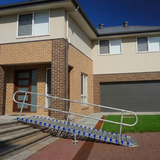 A metal stair ramp with blue grip pads and silver metal handrails installed on the front steps of a residential house.
