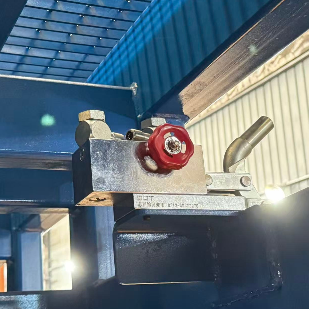 Closeup of a hydraulic control unit with a red handwheel and metal lever mounted beneath a blue grated forklift loading ramp.