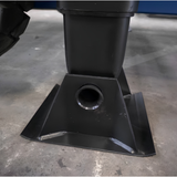 A close-up of a black metal mounting bracket or base with a circular opening, photographed on a concrete floor.