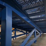 A close-up view of a large blue steel support structure with angled beams and a grid-like ceiling inside a warehouse or industrial space.