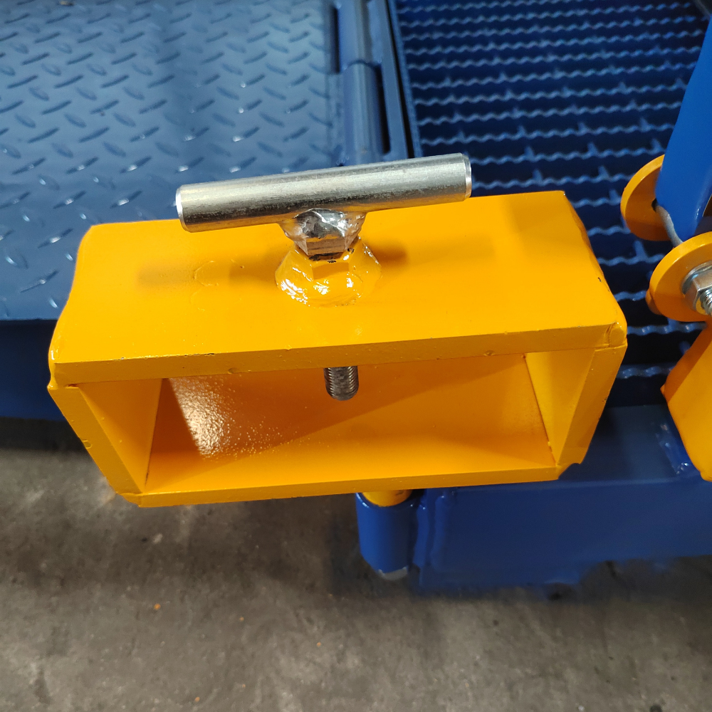 A close-up of a bright yellow metal clamp or bracket with a silver T-handle bolt, attached to a blue industrial platform or ramp.