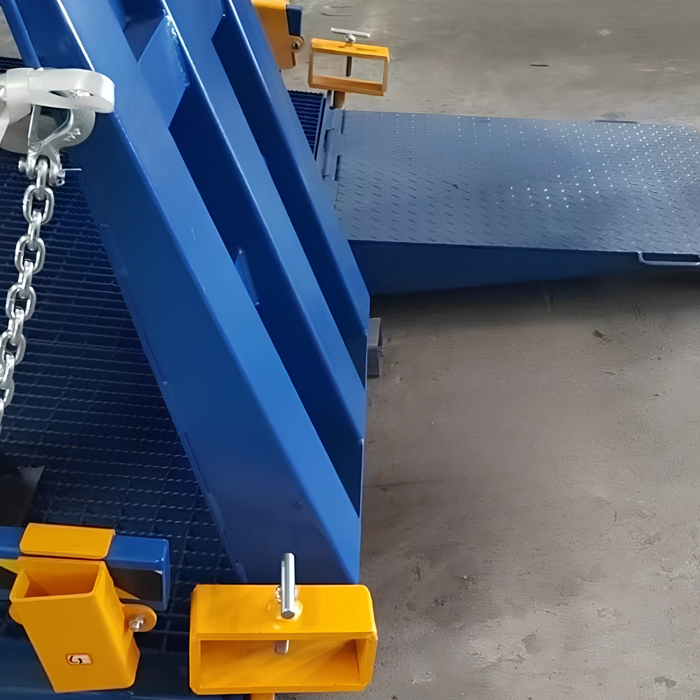 A close-up of a blue industrial metal ramp or vehicle access system with yellow safety blocks and a chain, photographed in a warehouse or workshop setting on a concrete floor.