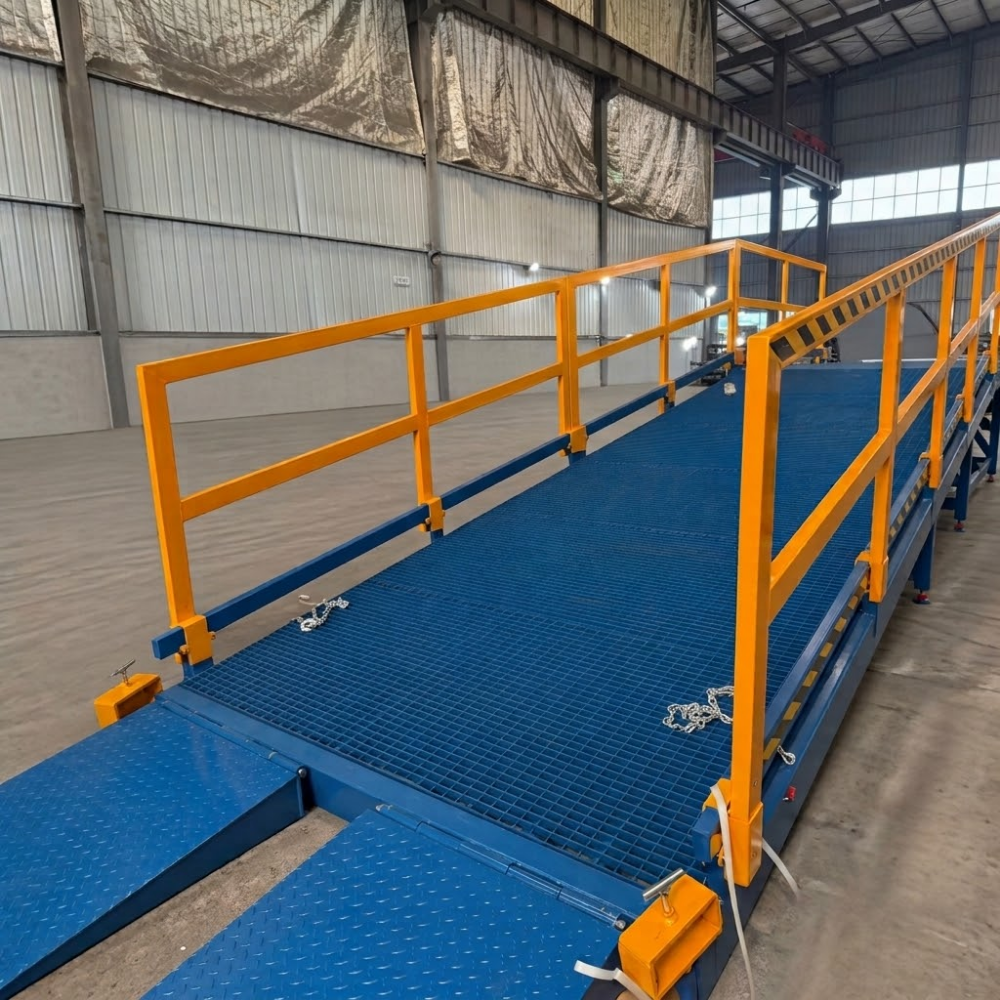A blue metal inclined yard ramp with bright yellow safety railings, shown inside a large warehouse or industrial building.