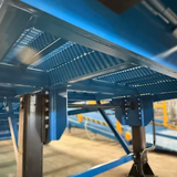Close-up of a blue metal industrial structure with slatted panels and support beams in a workshop or factory setting.