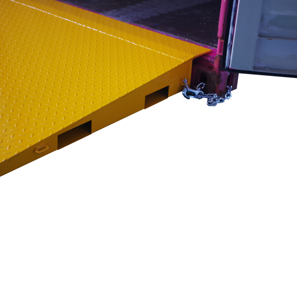Side close up view of a yellow Heeve self-supporting forklift container ramp placed in front of an open shipping container, showing the forklift tyne slots and the anti-skid surface.
