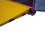 Side close up view of a yellow Heeve self-supporting forklift container ramp placed in front of an open shipping container, showing the forklift tyne slots and the anti-skid surface.
