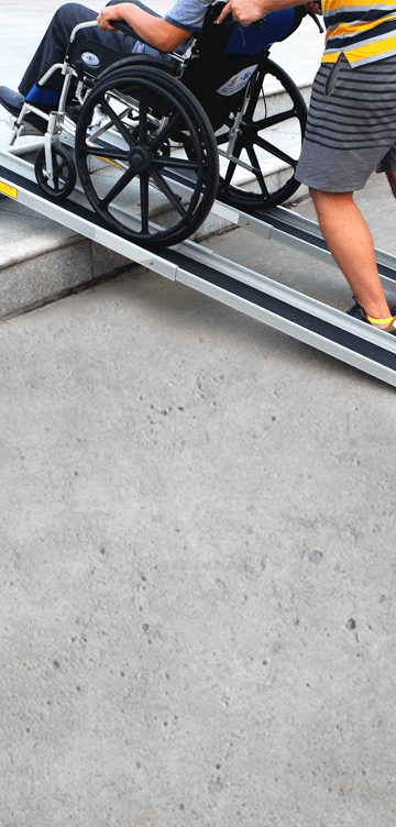 Man pushing a wheelchair up telescopic wheelchair ramps up concrete steps