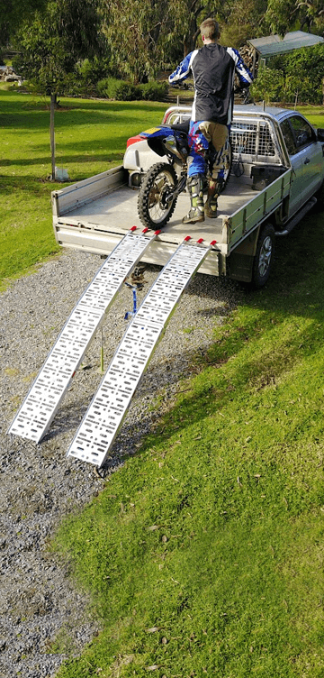 Man on ute with motorcycle using two loading ramps