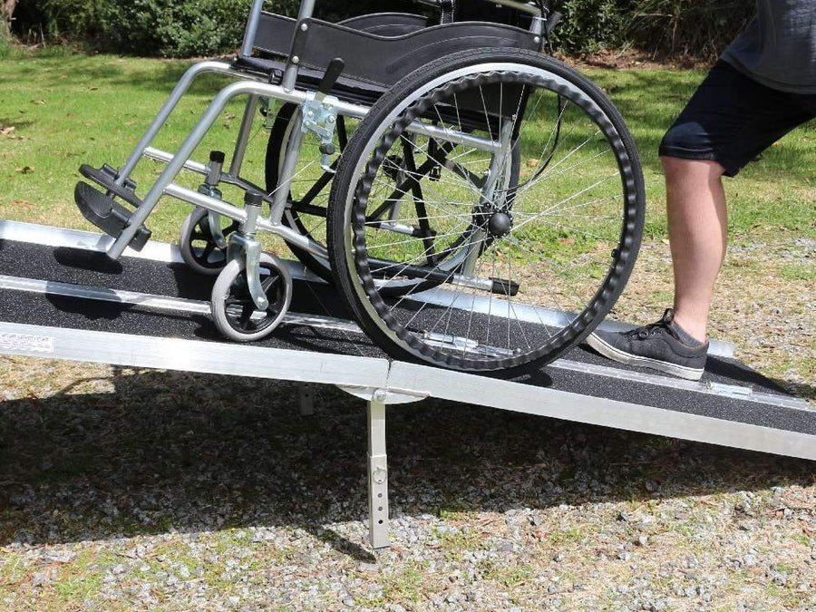 Helper pushing a wheelchair up a long multi-fold ramp on a lawn