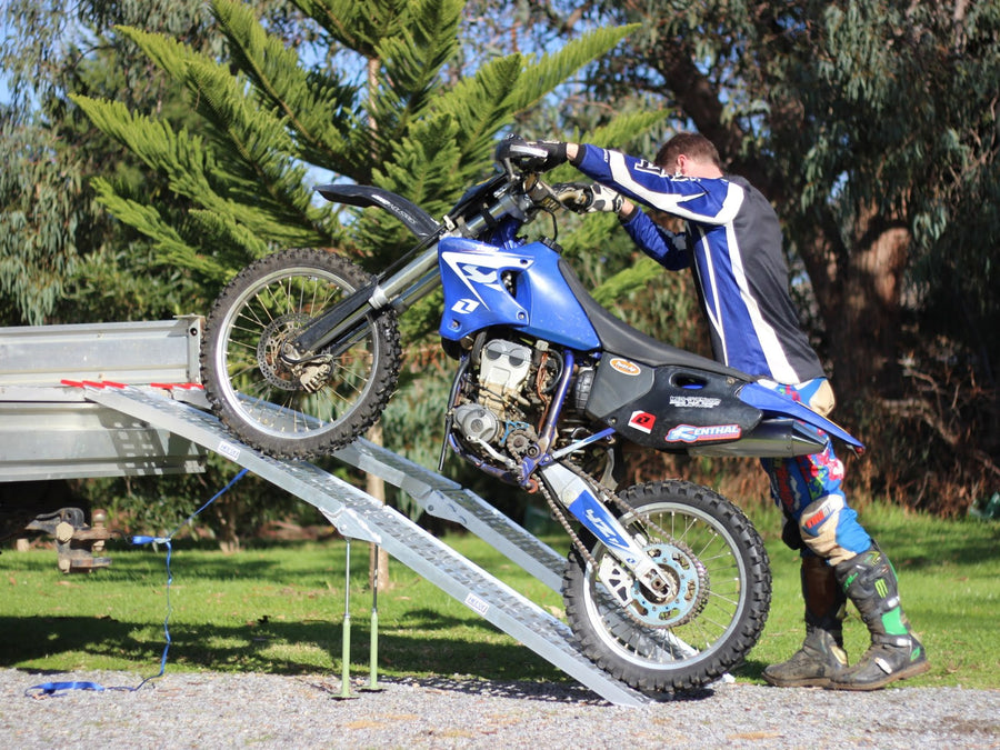 Rider walking beside the ramp pushing a dirt bike up a Heeve folding motorcycle ramp onto a ute