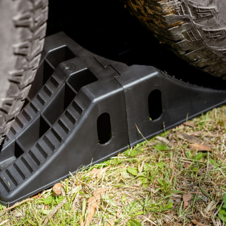 Black tire jack on grass with a vehicle tire in the background