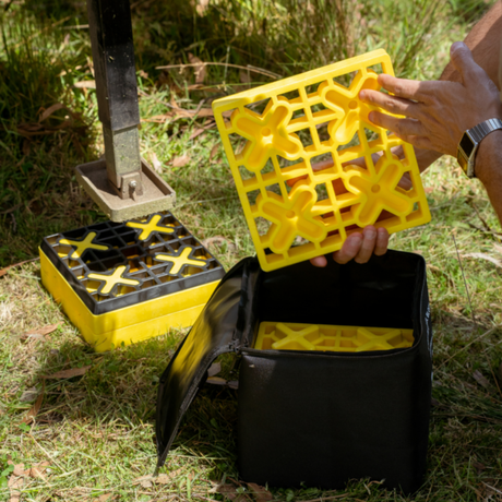 Yellow plastic grid being placed into a black container on grass