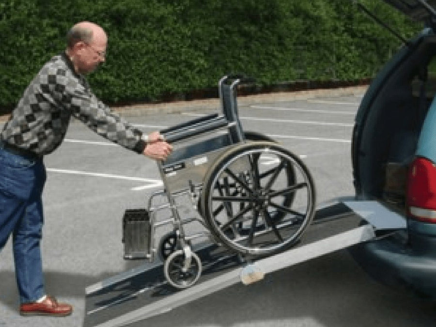 Man pushing a wheelchair up a folding ramp into a car