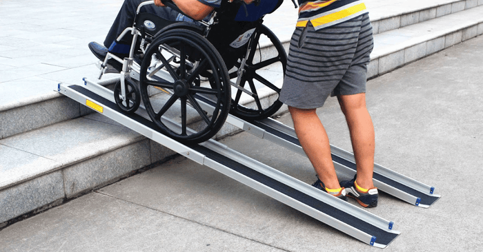 Two telescopic wheelchair ramps against concrete steps with a person in a wheelchair being pushed by another person 