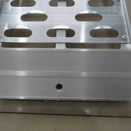Close-up of perforated holes and grooves on an aluminium ramp surface.