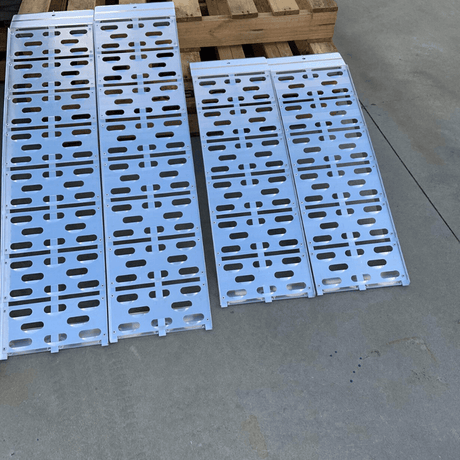 Two aluminium curved ramps in use on a grassy surface, propped up for loading.